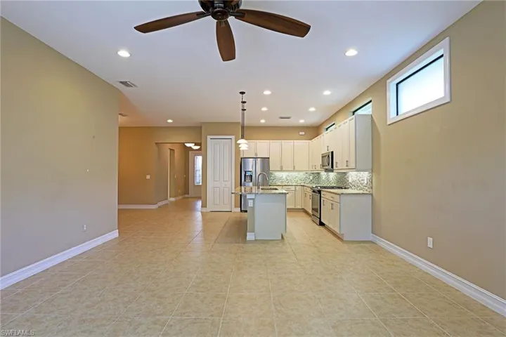 Kitchen with an island with sink, stainless steel appliances, backsplash, hanging light fixtures, and light stone countertops