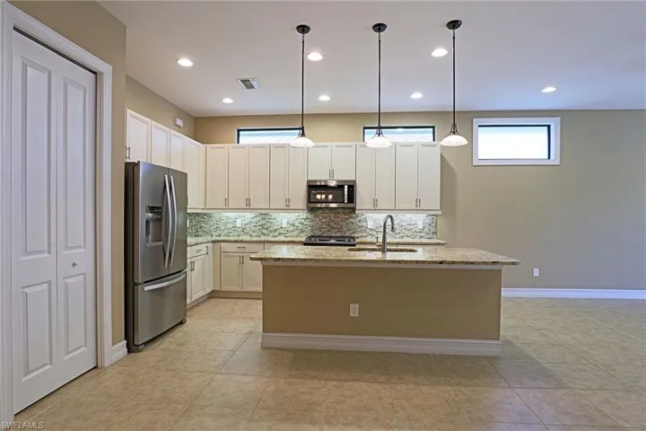 Kitchen featuring stainless steel appliances, backsplash, light stone counters, a center island with sink, and pendant lighting
