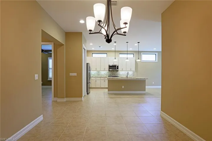 Kitchen with a kitchen island with sink, white cabinets, suspended lighting, decorative backsplash, and light tile patterned floors