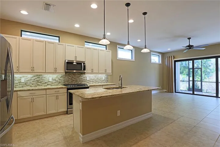 Kitchen with a center island with sink, stainless steel appliances, light stone counters, decorative backsplash, and decorative light fixtures