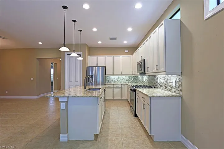 Kitchen with stainless steel appliances, light stone counters, white cabinetry, and decorative backsplash