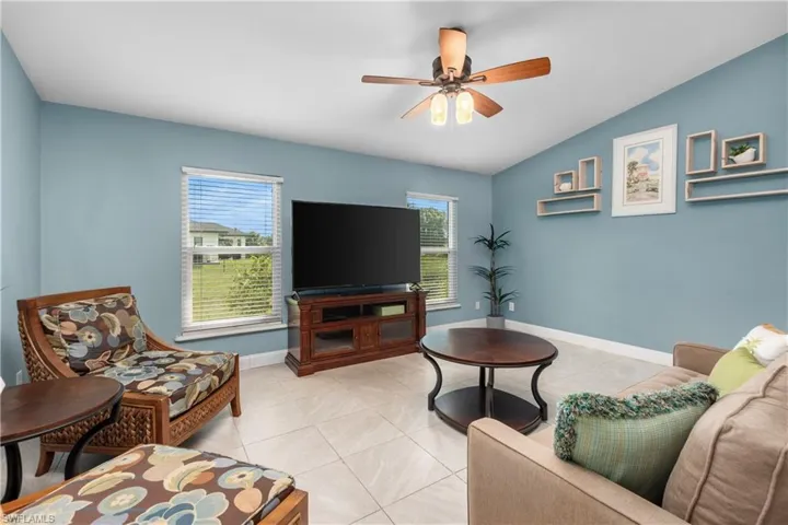 Living area with vaulted ceiling, plenty of natural light, a ceiling fan, and light tile patterned floors