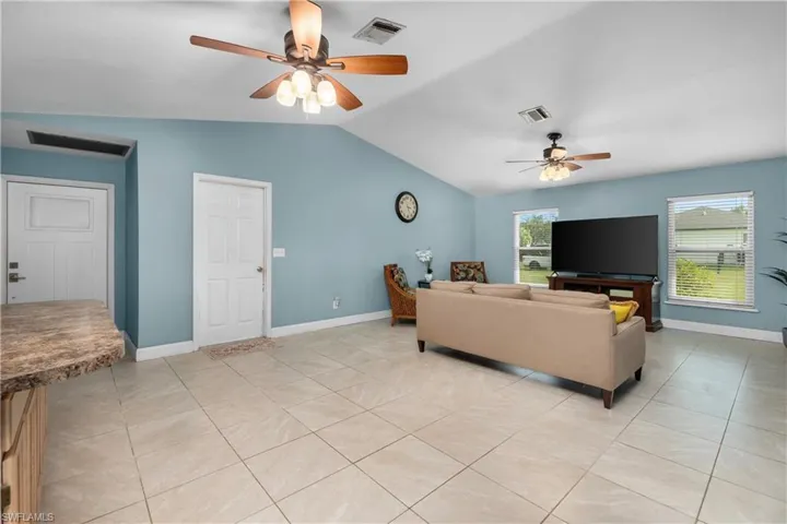 Living room featuring vaulted ceiling, light tile patterned floors, and a ceiling fan