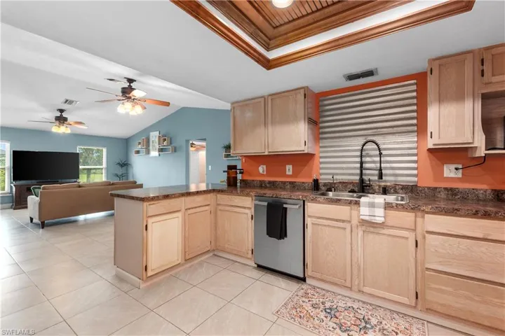 Kitchen with light brown cabinets, dark countertops, a raised ceiling, a peninsula, and ornamental molding