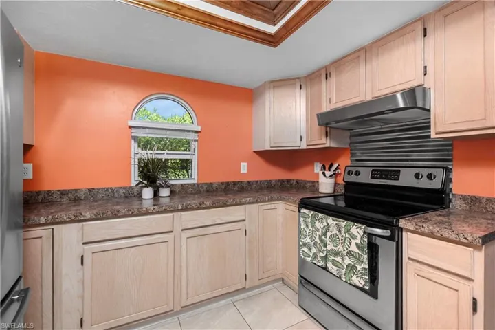 Kitchen with light brown cabinets, stainless steel appliances, dark countertops, and under cabinet range hood
