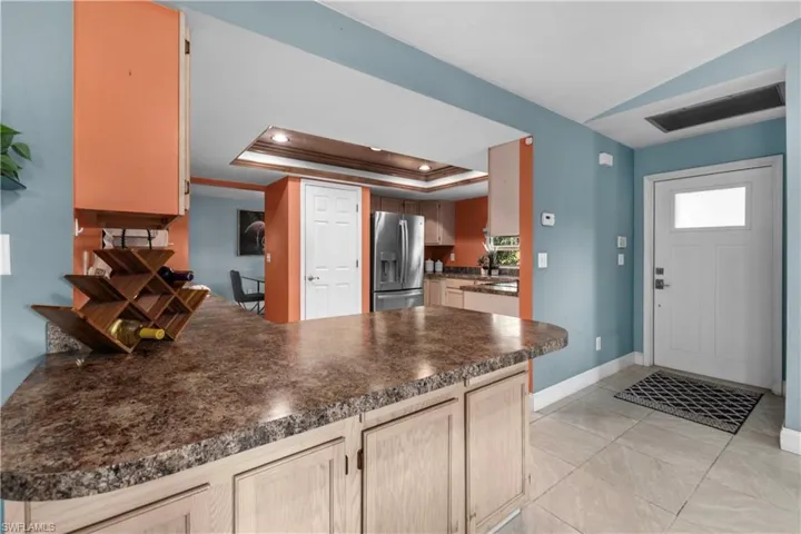Kitchen featuring a tray ceiling, stainless steel fridge, dark countertops, a peninsula, and light tile patterned floors
