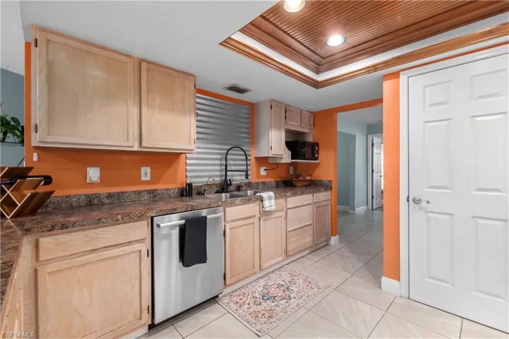 Kitchen with light brown cabinets, dark countertops, stainless steel dishwasher, crown molding, and a raised ceiling