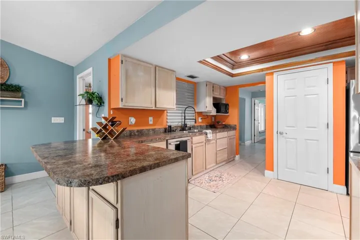 Kitchen featuring light brown cabinets, dark countertops, a peninsula, light tile patterned floors, and a tray ceiling
