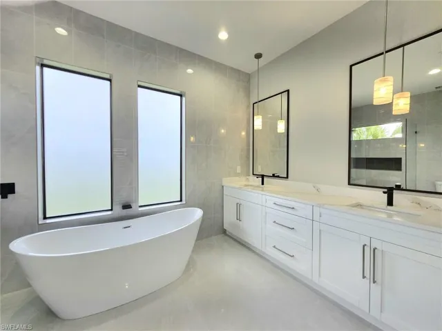 Bathroom with tile patterned floors, a tub, vanity, and tile walls