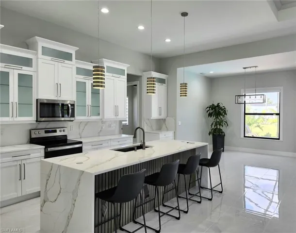 Kitchen featuring sink, appliances with stainless steel finishes, decorative backsplash, a kitchen island with sink, and light tile patterned floors