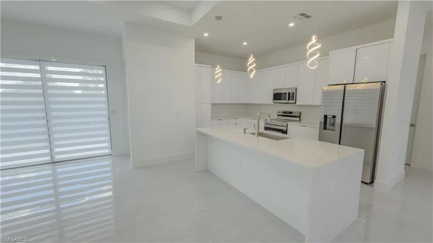 Kitchen with appliances with stainless steel finishes, white cabinets, light stone countertops, recessed lighting, and hanging light fixtures