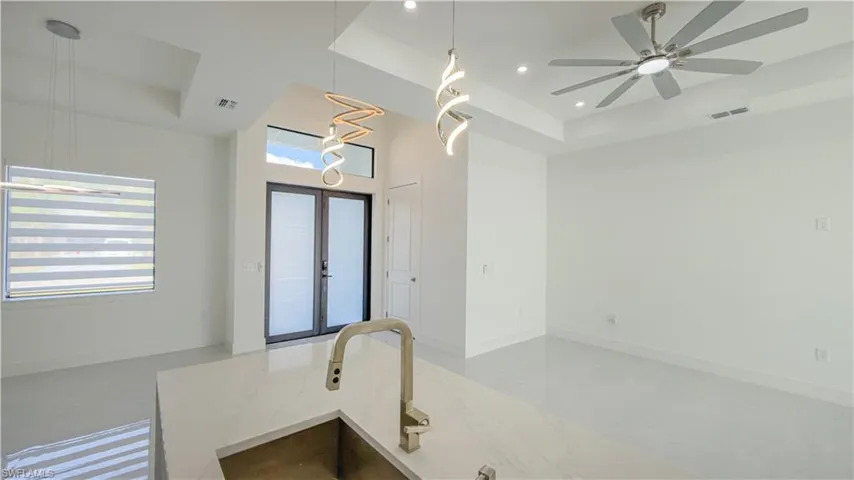 Kitchen featuring a tray ceiling, decorative light fixtures, open floor plan, french doors, and light stone counters