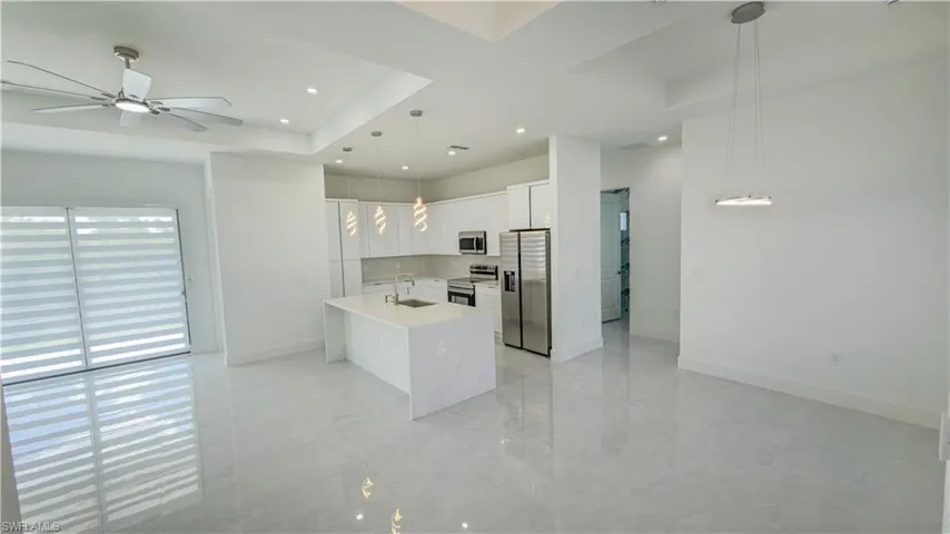 Kitchen featuring white cabinets, appliances with stainless steel finishes, hanging light fixtures, light stone countertops, and a tray ceiling