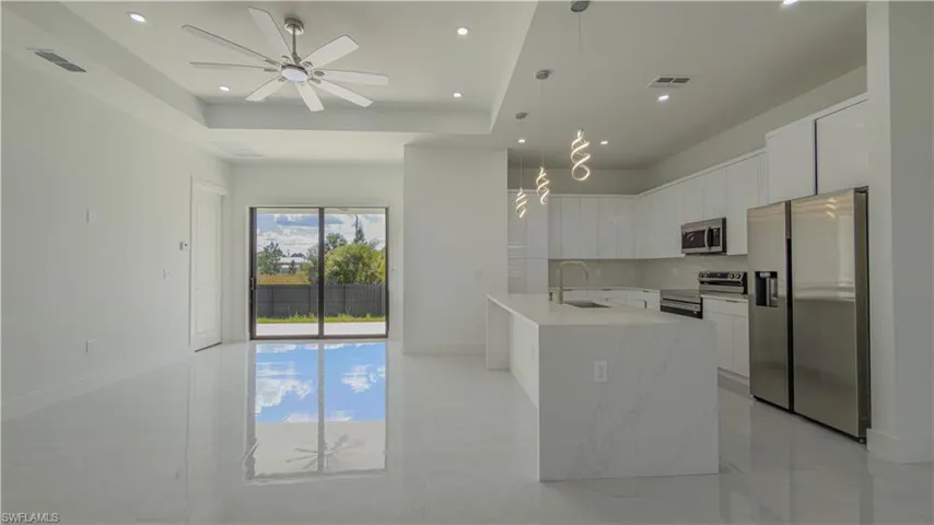 Kitchen with appliances with stainless steel finishes, white cabinetry, pendant lighting, light stone countertops, and decorative backsplash