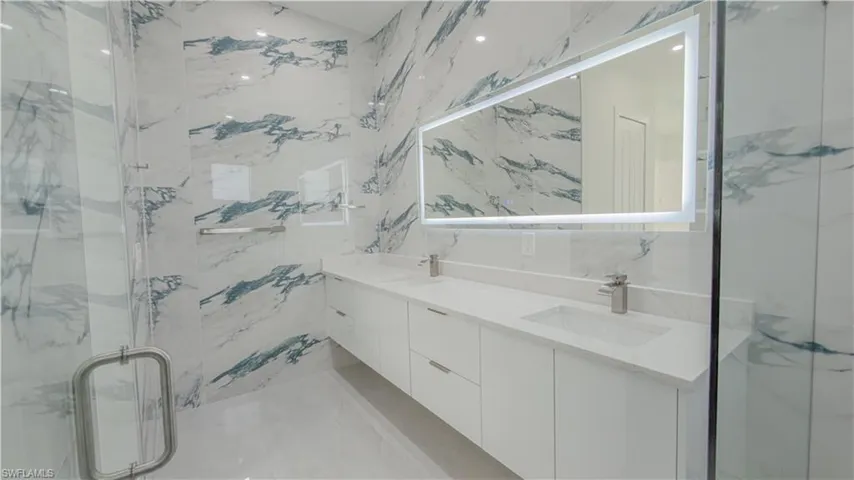 Full bath with double vanity and a marble finish shower