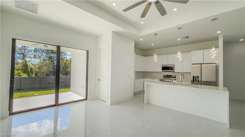 Kitchen with white cabinets, appliances with stainless steel finishes, pendant lighting, a kitchen island with sink, and backsplash