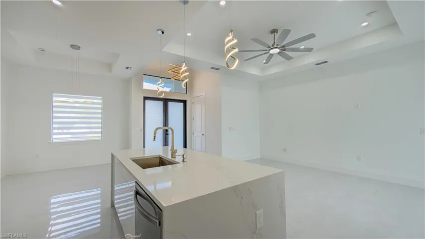 Kitchen with a raised ceiling, light stone counters, hanging light fixtures, dishwasher, and open floor plan