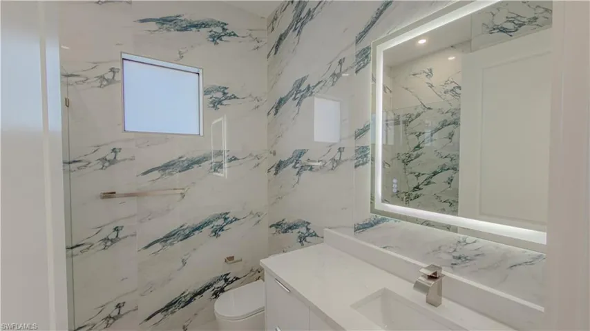 Bathroom featuring vanity, a marble finish shower, and stone wall