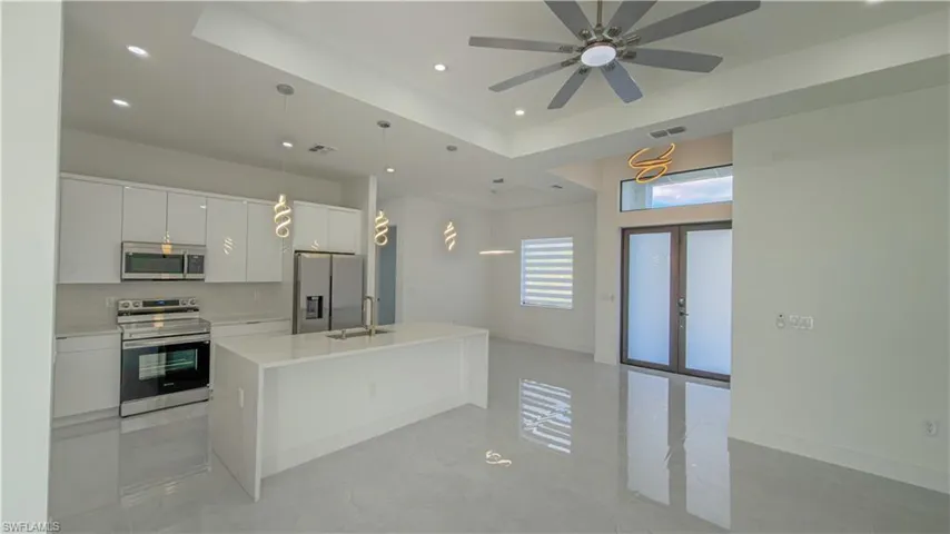 Kitchen featuring appliances with stainless steel finishes, a center island with sink, hanging light fixtures, white cabinets, and recessed lighting