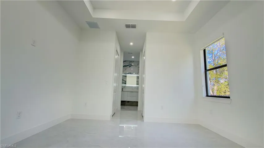 Unfurnished room featuring a tray ceiling, recessed lighting, and light marble finish flooring