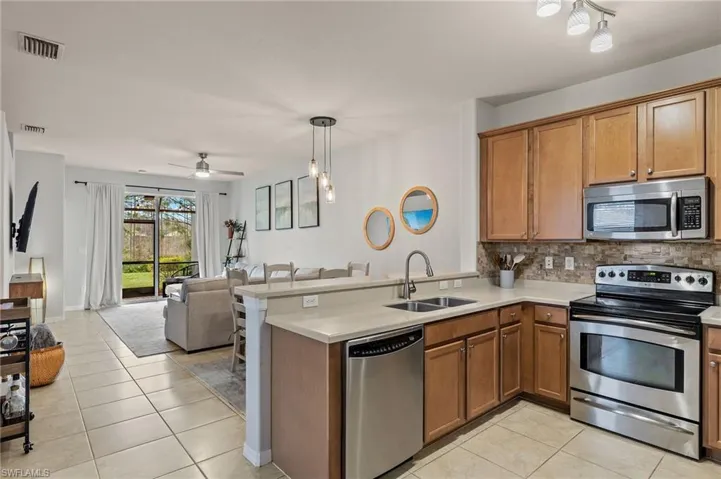 Kitchen with kitchen peninsula, sink, light tile patterned flooring, backsplash, and appliances with stainless steel finishes