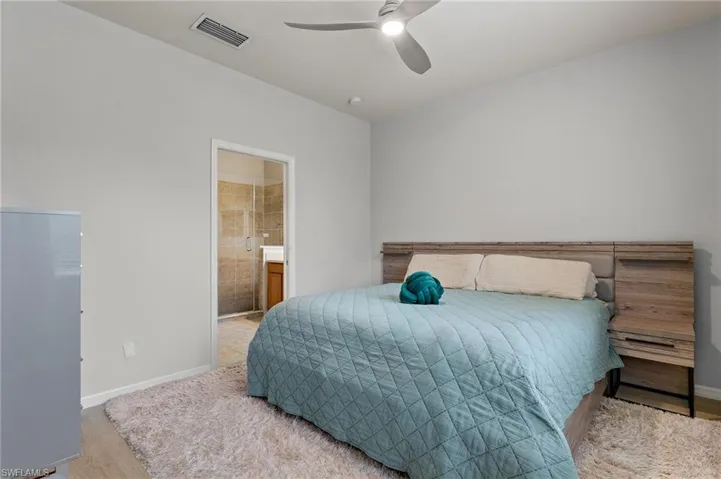 Bedroom with ensuite bathroom, ceiling fan, and light hardwood / wood-style flooring