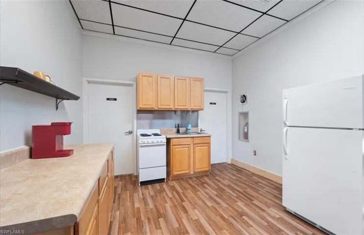 Kitchen with white appliances, light countertops, open shelves, light wood-type flooring, and light brown cabinetry