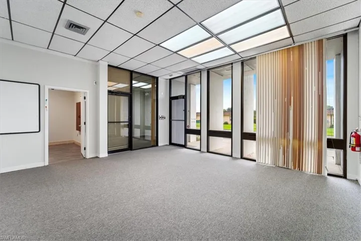 Carpeted empty room featuring a wall of windows and a drop ceiling