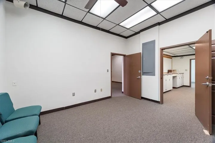 Empty room with light colored carpet, a ceiling fan, a paneled ceiling, and electric panel