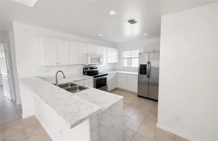 Kitchen featuring stainless steel appliances, white cabinets, a peninsula, light stone counters, and recessed lighting