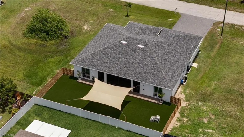 Contemporary-style home featuring a gray shingle roof and a spacious, fenced backyard with sunshade and turfing