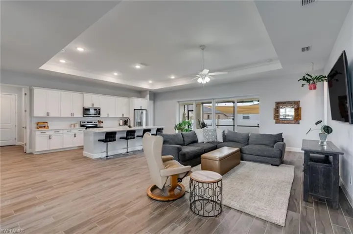 Open-concept living area featuring wood-look tile flooring, a tray ceiling with recessed lighting, and a ceiling fan