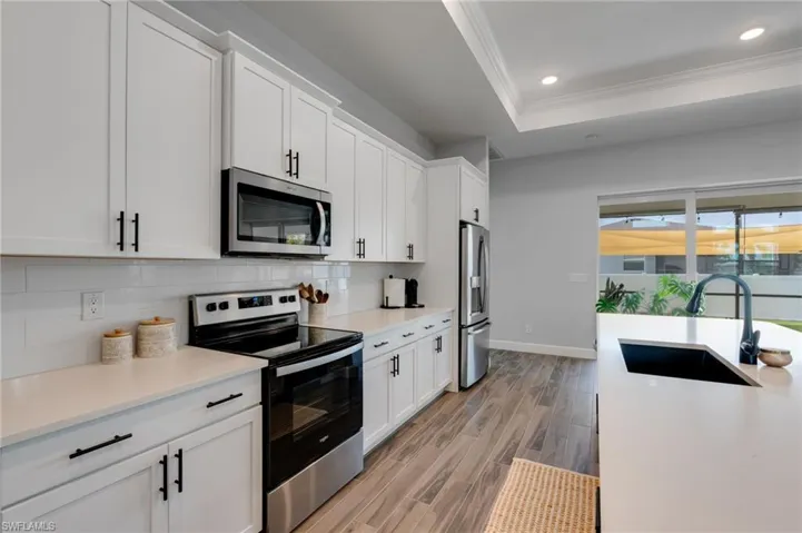 Contemporary kitchen featuring white shaker cabinetry, stainless steel appliances, and wood-finish flooring