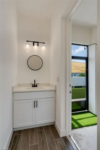 Compact vanity area featuring wood-finish flooring and a white shaker-style cabinet with black hardware. Serves as a great future pool bath!