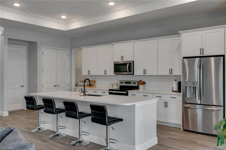 Modern kitchen featuring an expansive center island with seating, white shaker cabinetry, stainless steel appliances, and wood-finish flooring