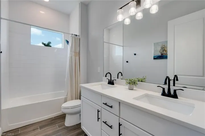 Bathroom featuring a white dual vanity with undermount sinks and black fixtures. Tub shower combo.