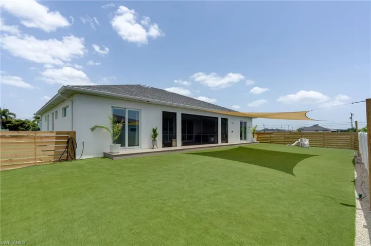 Expansive artificial turf backyard featuring a modern stucco exterior, sliding glass doors, a patio area, and a horizontal slat fence