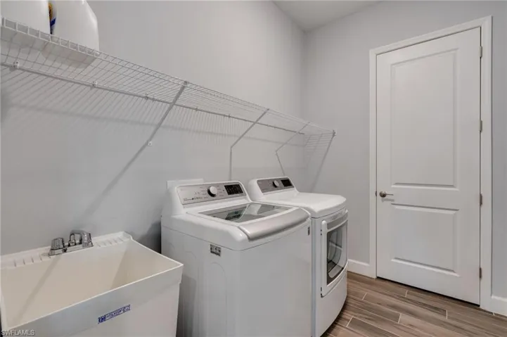 Dedicated laundry room featuring light gray walls, wood-finish tile flooring, a built-in utility sink with chrome faucet, and white wire shelving
