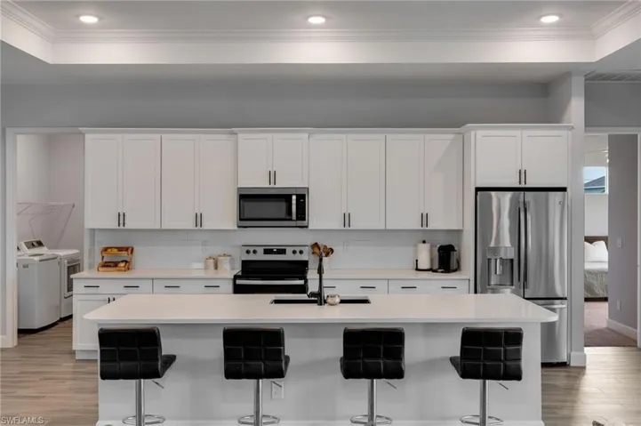 Modern kitchen featuring white shaker cabinetry, stainless steel appliances, a center island with seating, a subway tile backsplash, and recessed lighting