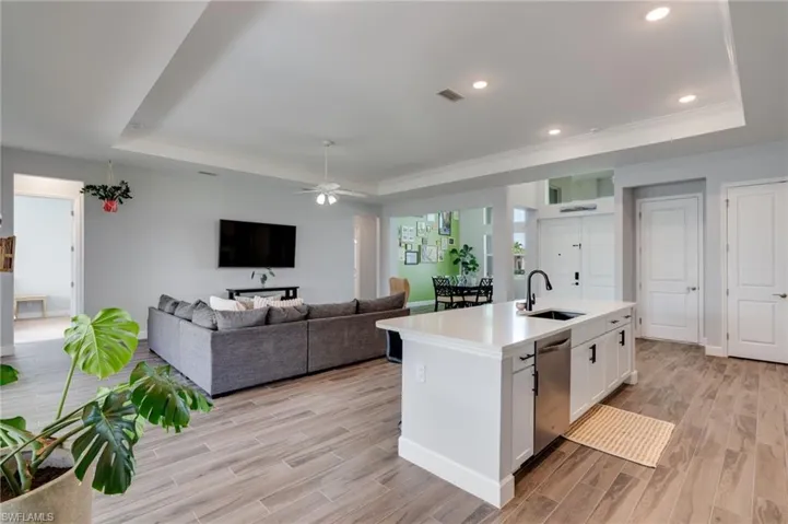 Open-concept living space featuring wood-finish flooring, a kitchen island with a sink and dishwasher, recessed lighting, a ceiling fan, and tray ceilings