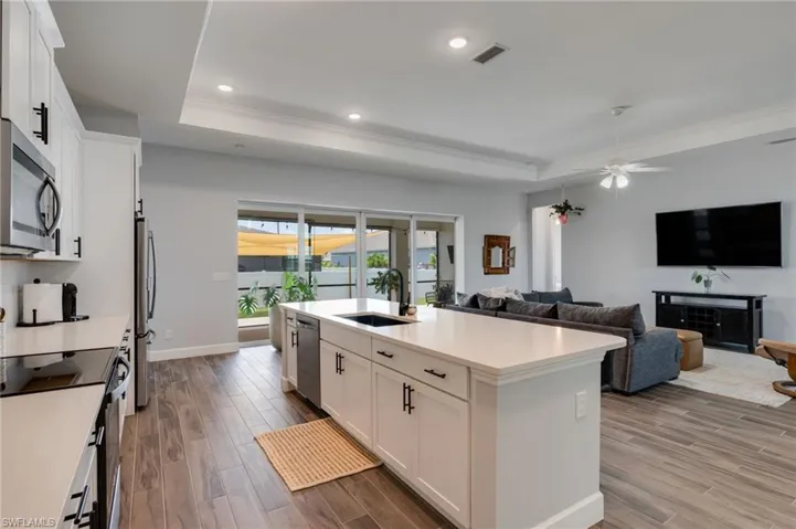 Spacious kitchen featuring an island with a sink, stainless steel appliances, white cabinetry with black hardware, and wood-finish flooring