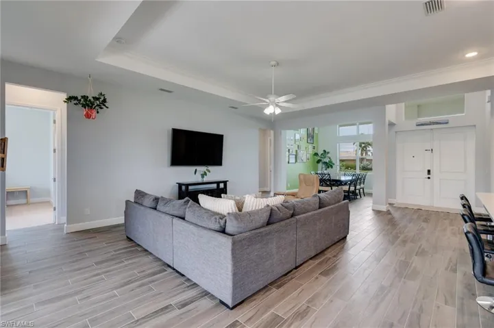 Open-concept living area featuring wood-finish tile flooring, a tray ceiling with recessed lighting, and a ceiling fan