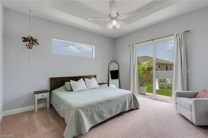 Primary bedroom. Tray ceiling with a ceiling fan, transom window, and sliding glass doors to the exterior