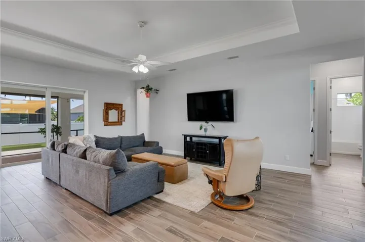 Living area featuring wood-finish flooring, a tray ceiling with a ceiling fan, and sliding glass doors to the exterior