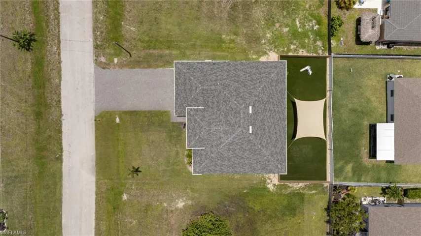 Property featuring an asphalt shingle roof, a paver driveway, and a fenced rear yard with artificial turf and a sunshade