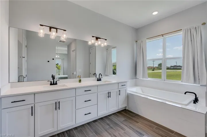 Bathroom with a dual vanity featuring white shaker cabinetry, quartz countertops, and matte black fixtures