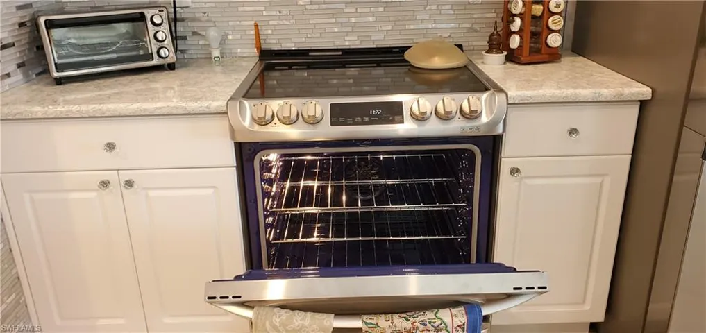 Room details with decorative backsplash, white cabinetry, a toaster, and stainless steel electric range oven