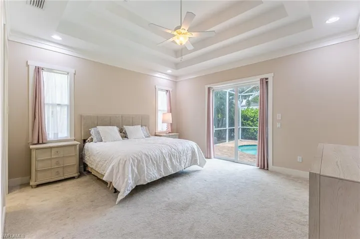 Primary bedroom with crown molding, multi layered tray ceiling, recessed lighting, and hurricane impact windows and sliders.