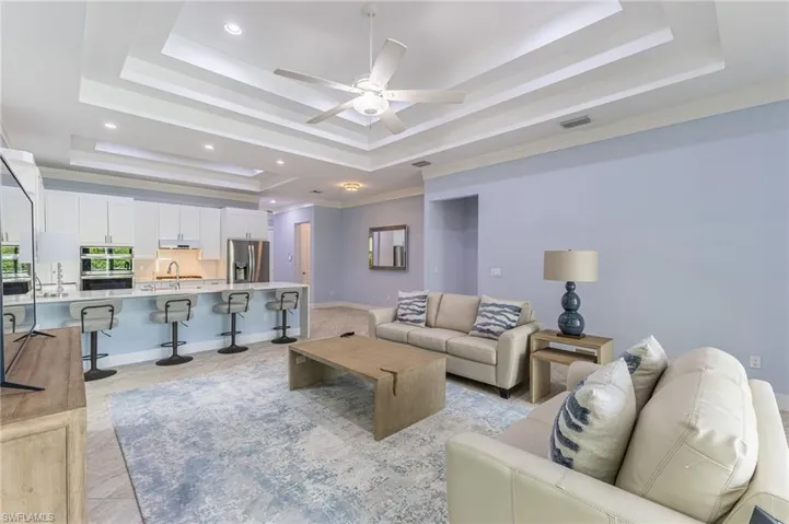 Living area with a raised ceiling, ceiling fan, crown molding, and recessed lighting.