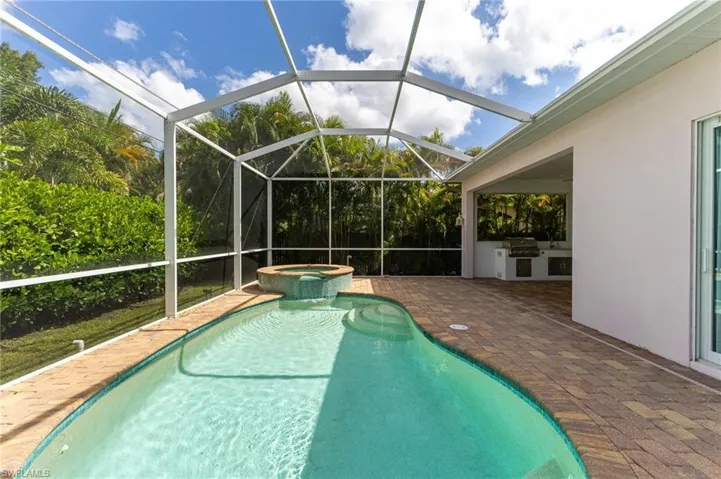 View of swimming pool with a lanai, a sunroom, a pool with connected hot tub, an outdoor kitchen, and a patio area